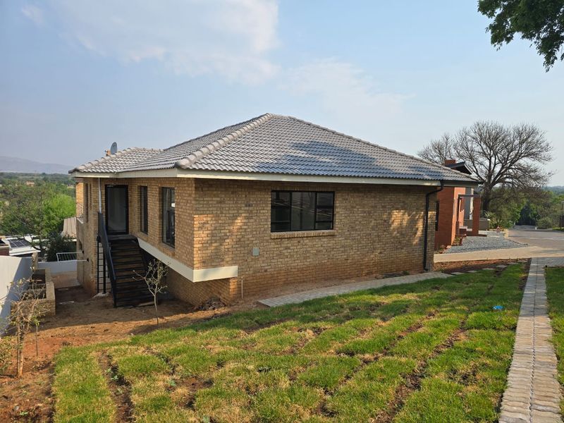 Rear view of a brick house featuring a tiled roof, metal staircase, and a paved walkway leading through the garden area.