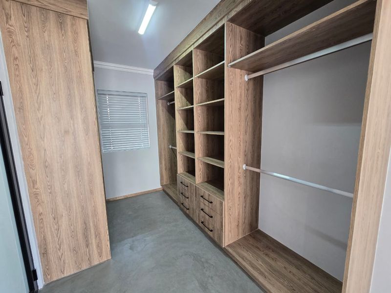 A modern walk-in closet featuring extensive built-in wood-grain cabinetry with ample shelving, hanging space, and drawers, complemented by polished concrete flooring.