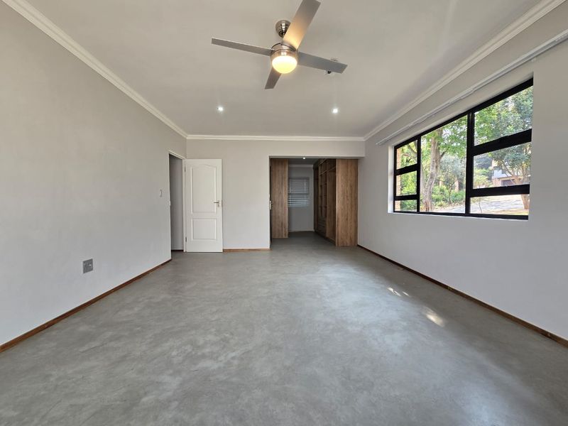 Spacious bedroom featuring polished concrete floors, built-in wooden cupboards, a ceiling fan, and large windows providing natural light.