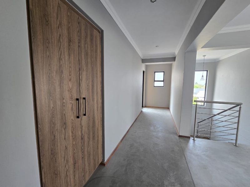 A bright, modern hallway featuring polished concrete flooring, a built-in wood-finish cupboard, and a stainless steel balustrade overlooking the staircase.