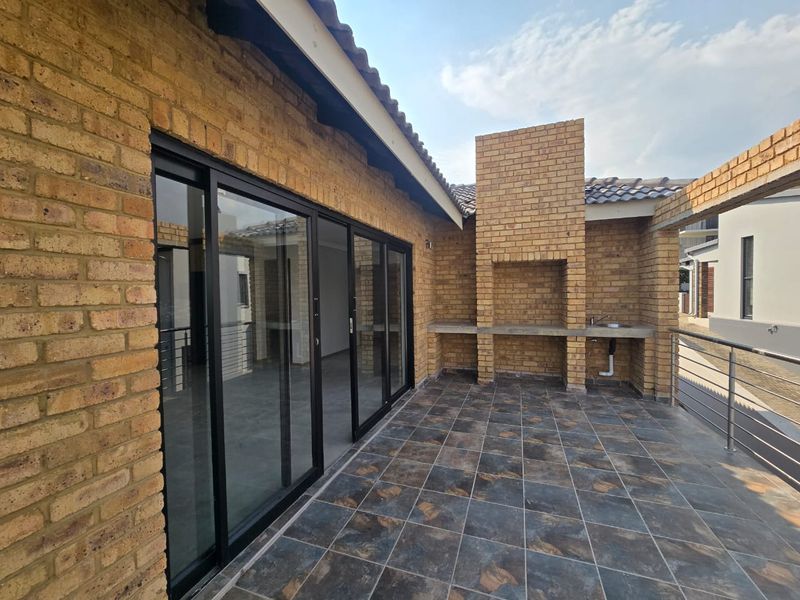 Covered patio featuring a built-in brick braai, concrete prep area with sink, tiled flooring, and large sliding glass doors leading to the interior.
