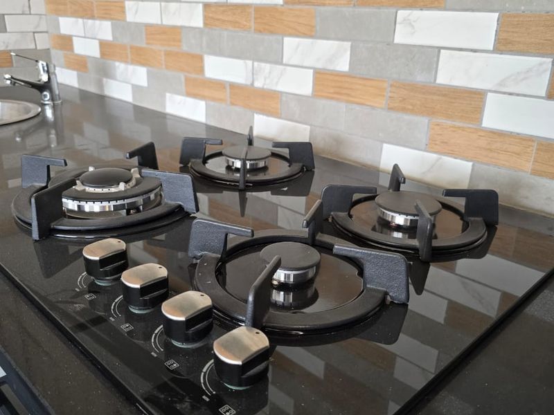 A modern kitchen featuring a black glass gas cooktop, stone countertops, and a decorative multi-toned tiled backsplash.