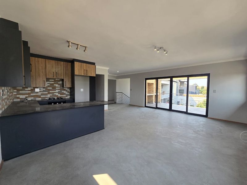 Spacious open-plan living area featuring a modern kitchen with dark cabinetry, stone countertops, and large sliding doors leading to an outdoor space.