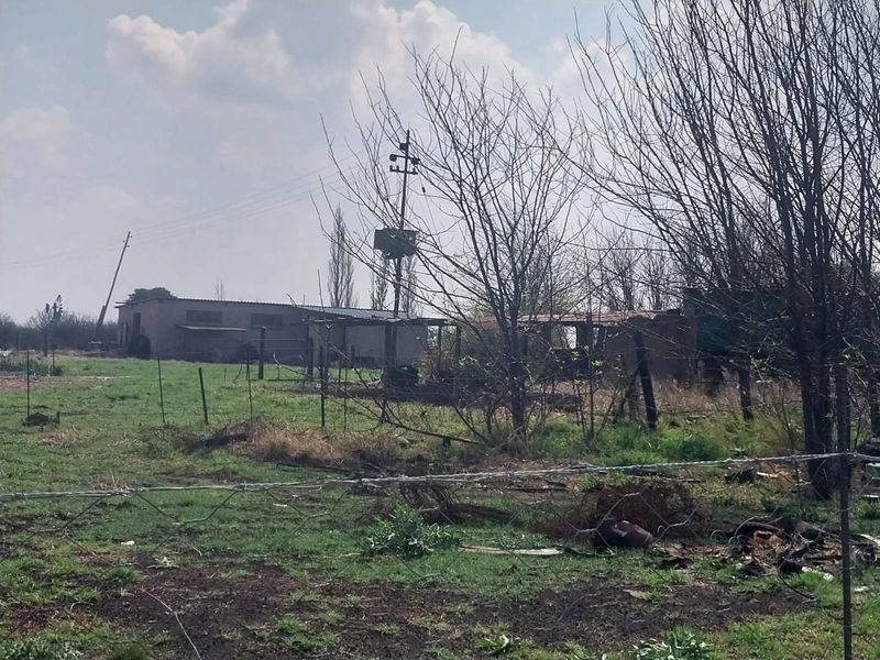 View of the small holding grounds featuring an outbuilding, utility infrastructure, and perimeter fencing in need of maintenance.