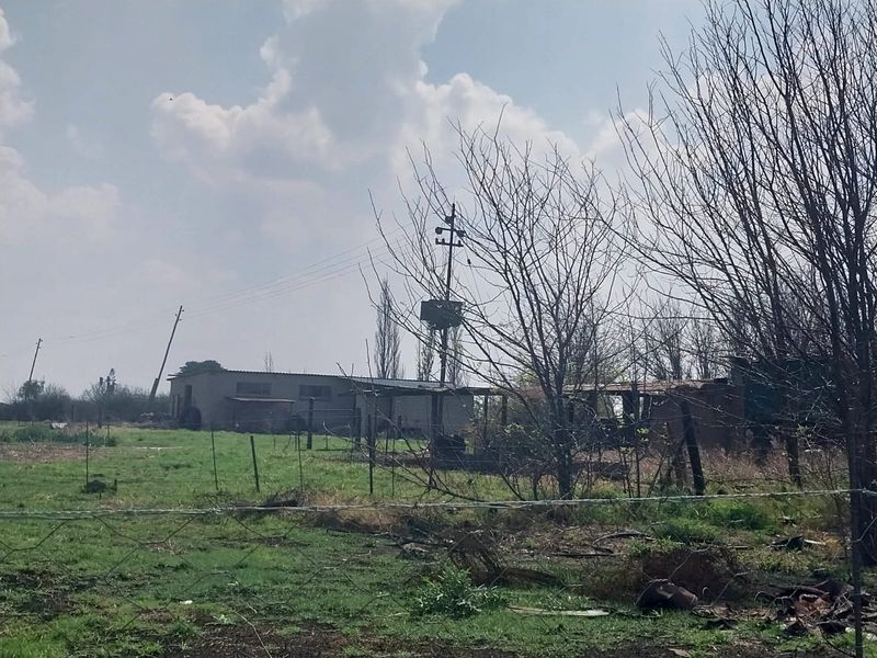 A view of the property grounds featuring an outbuilding, wire fencing, and utility infrastructure on a rural small holding.