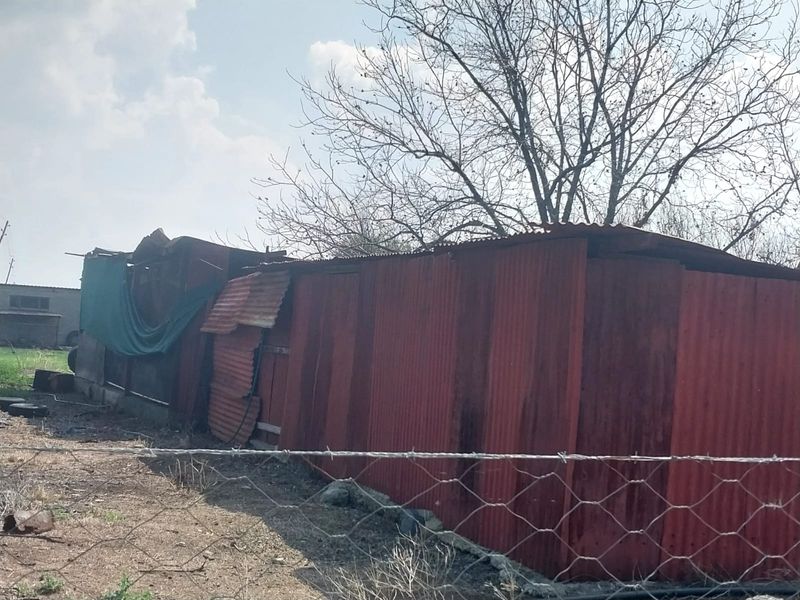 A view of a dilapidated outbuilding constructed from corrugated iron, showing significant signs of wear and structural damage.