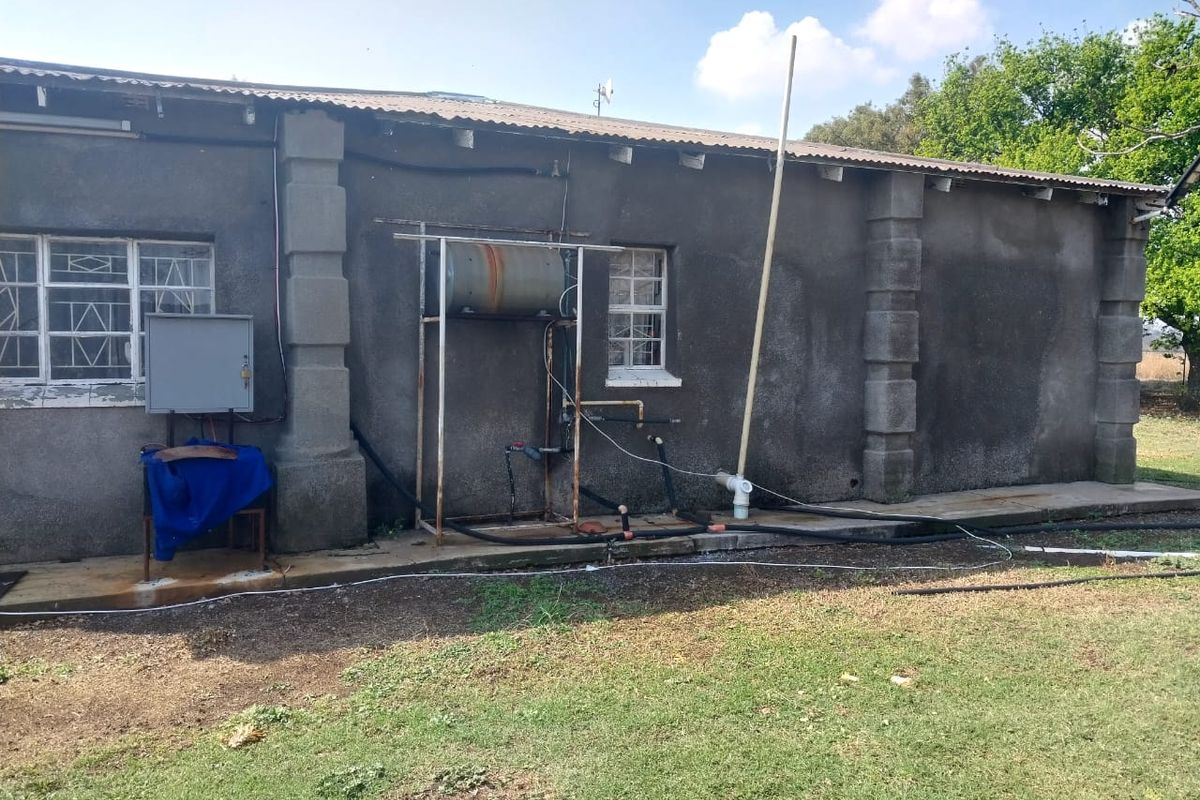 Rear exterior view of the property showing exposed plumbing, an external geyser unit, and weathered wall finishes.
