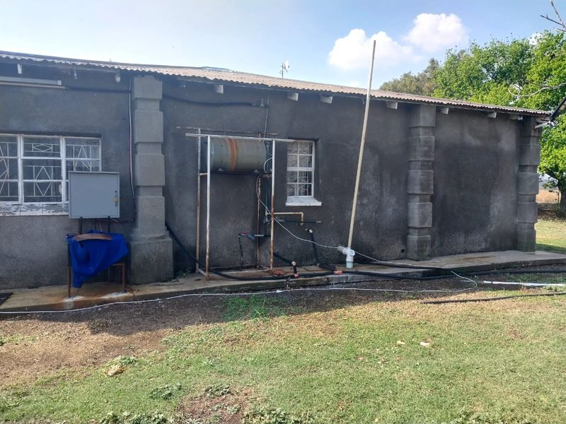 Rear exterior view of the property showing exposed plumbing, an external geyser unit, and weathered wall finishes.