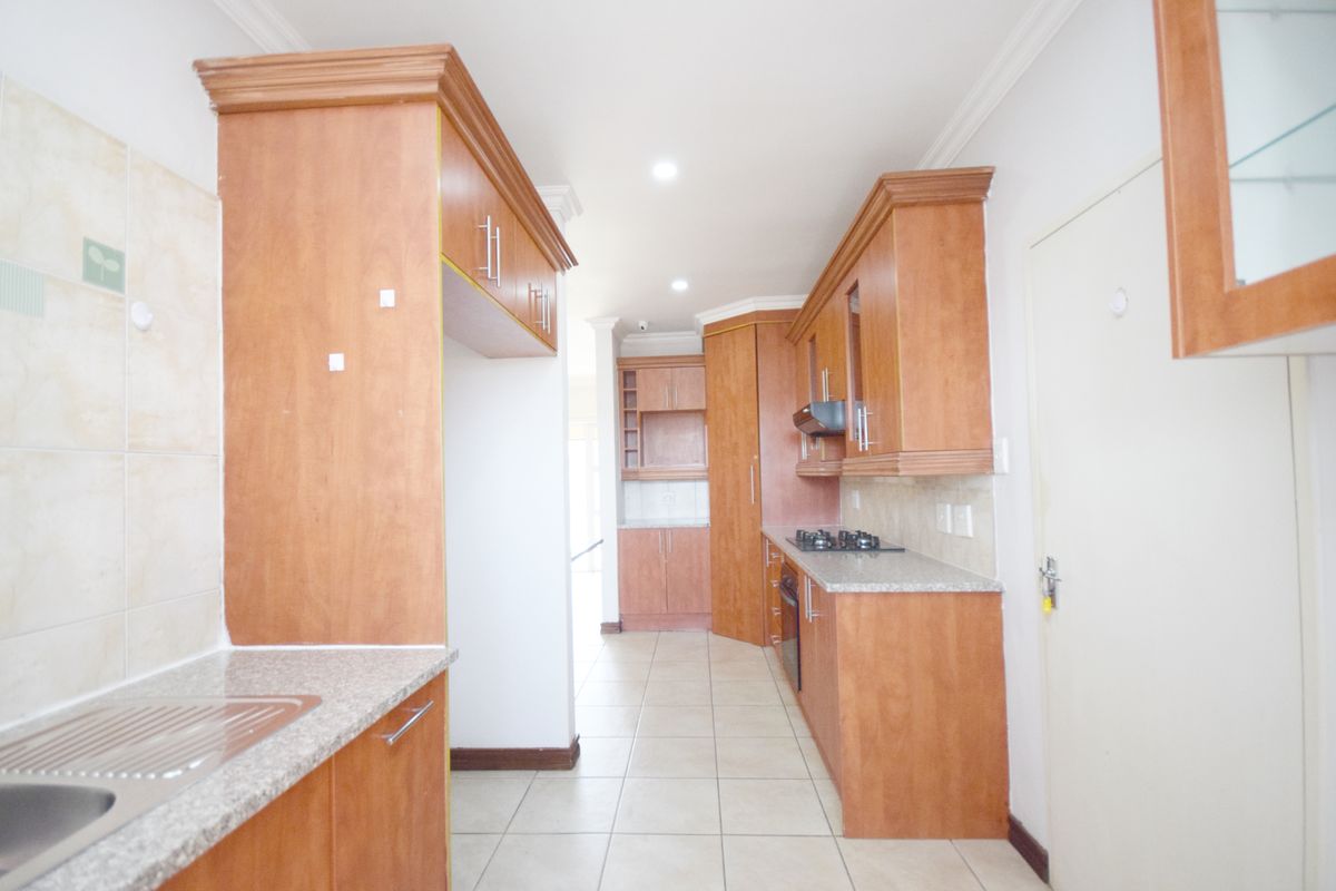 A functional kitchen featuring wooden cabinetry, granite countertops, a gas hob, and built-in oven, offering a clean and practical workspace.
