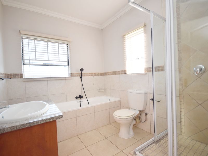 A clean, functional bathroom featuring a vanity with granite countertop, a bathtub, a separate shower enclosure, and neutral wall and floor tiling.