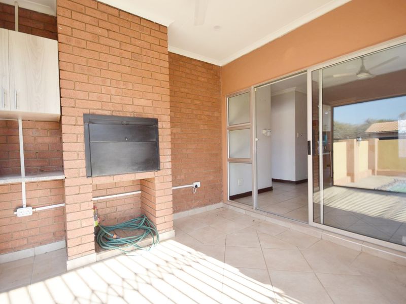 Covered patio area featuring a built-in brick braai, tiled flooring, and sliding glass doors providing access to the interior living space.