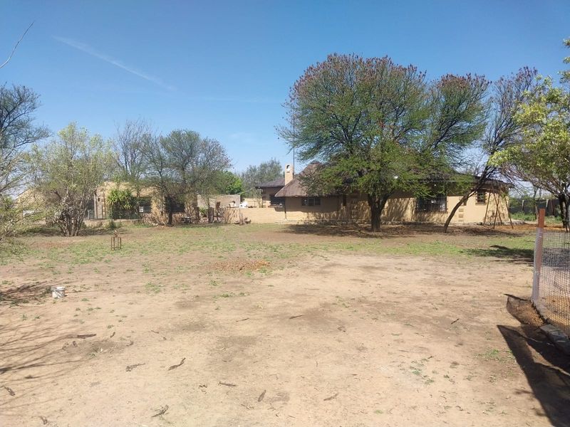 A view of the rear exterior of the small holding, featuring a traditional thatch-roofed dwelling set within a large, open garden area.