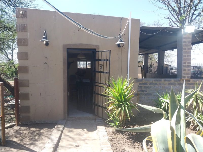 Rear exterior view of a small holding structure featuring a security gate, exterior lighting, and an adjacent covered patio area.