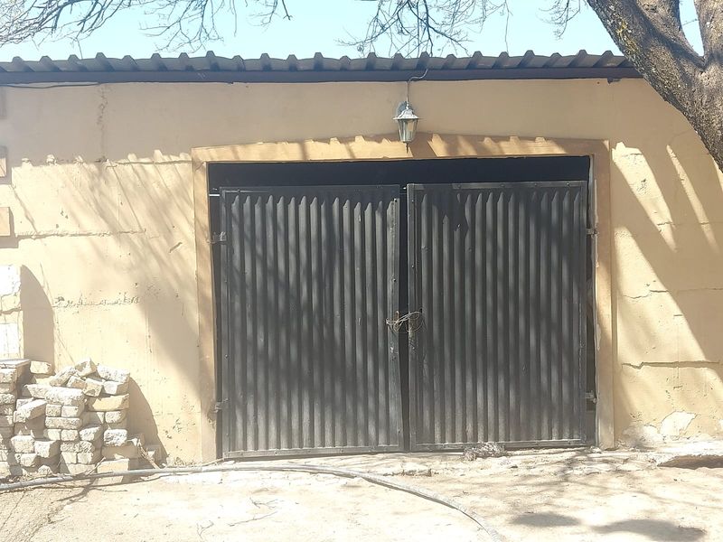 A detached garage structure featuring corrugated metal double doors and a simple exterior light fixture, showing signs of weathered plaster and paint.