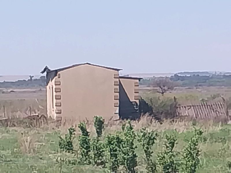 A distant view of a small holding structure with visible roof damage and surrounding fencing in a rural landscape setting.