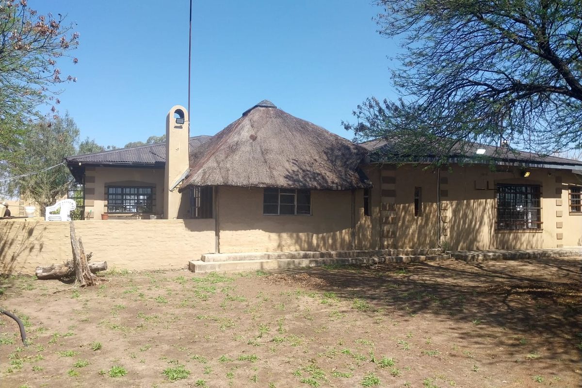 Rear view of a small holding dwelling featuring a combination of thatch and corrugated iron roofing with masonry walls and security bars.