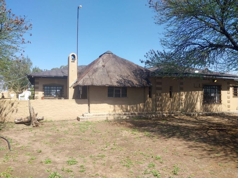 Rear view of a small holding dwelling featuring a combination of thatch and corrugated iron roofing with masonry walls and security bars.