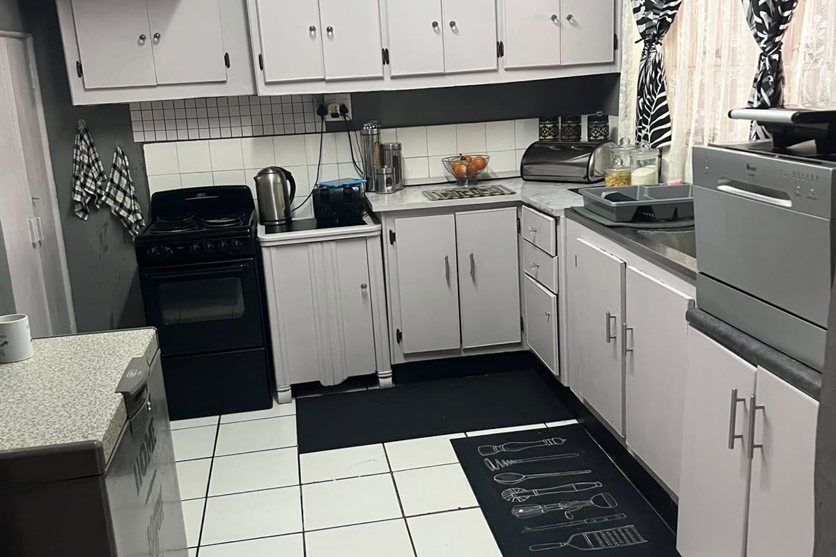 A functional kitchen featuring white cabinetry, tiled flooring, a tiled backsplash, and a freestanding stove, offering a practical layout for daily meal preparation.