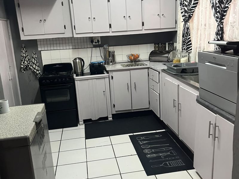 A functional kitchen featuring white cabinetry, tiled flooring, a tiled backsplash, and a freestanding stove, offering a practical layout for daily meal preparation.