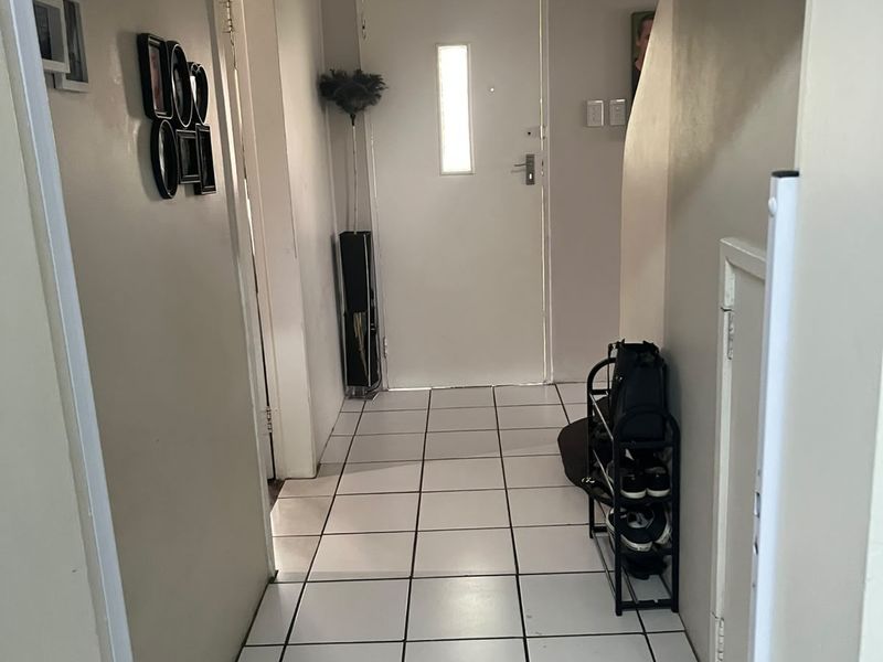 A functional entrance hallway featuring white tiled flooring and a secure front door, providing access to the rest of the home.
