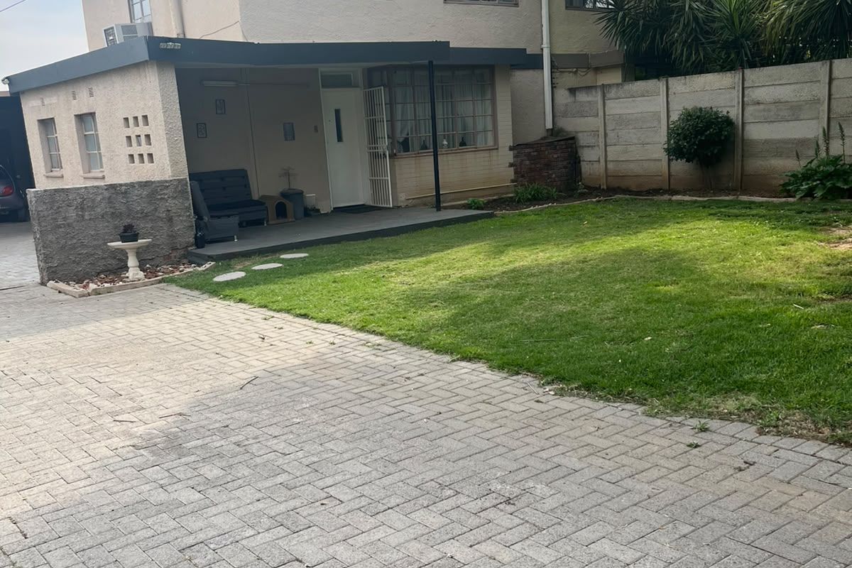 Rear view of a two-story house featuring a paved driveway, a covered patio area, and a private lawn enclosed by a precast concrete wall.