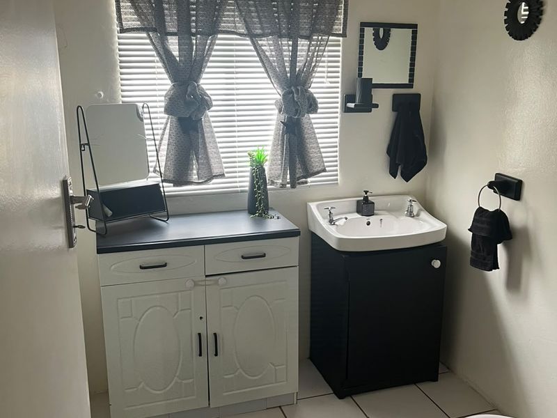 A functional bathroom featuring a vanity cabinet, washbasin, toilet, and tiled flooring with window blinds for privacy.