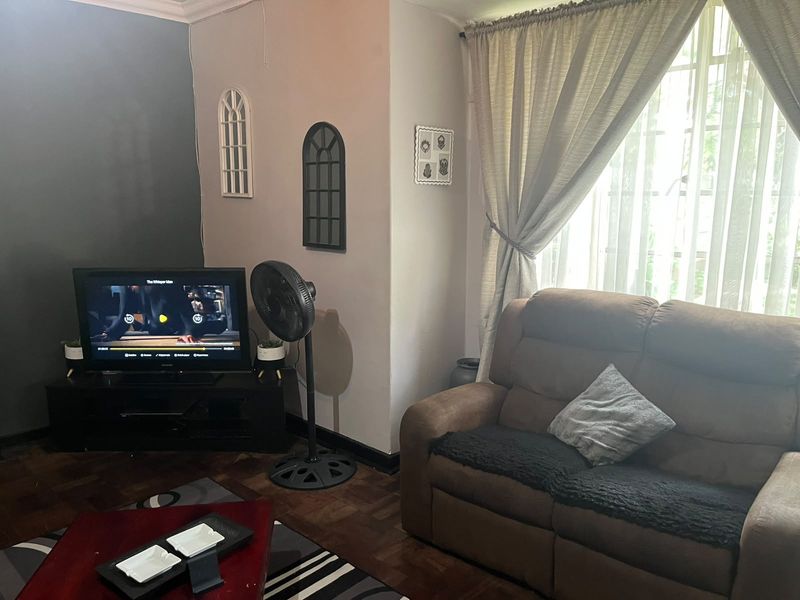 A cozy living room featuring classic parquet flooring and large windows with curtain treatments, providing a comfortable and functional space for relaxation.