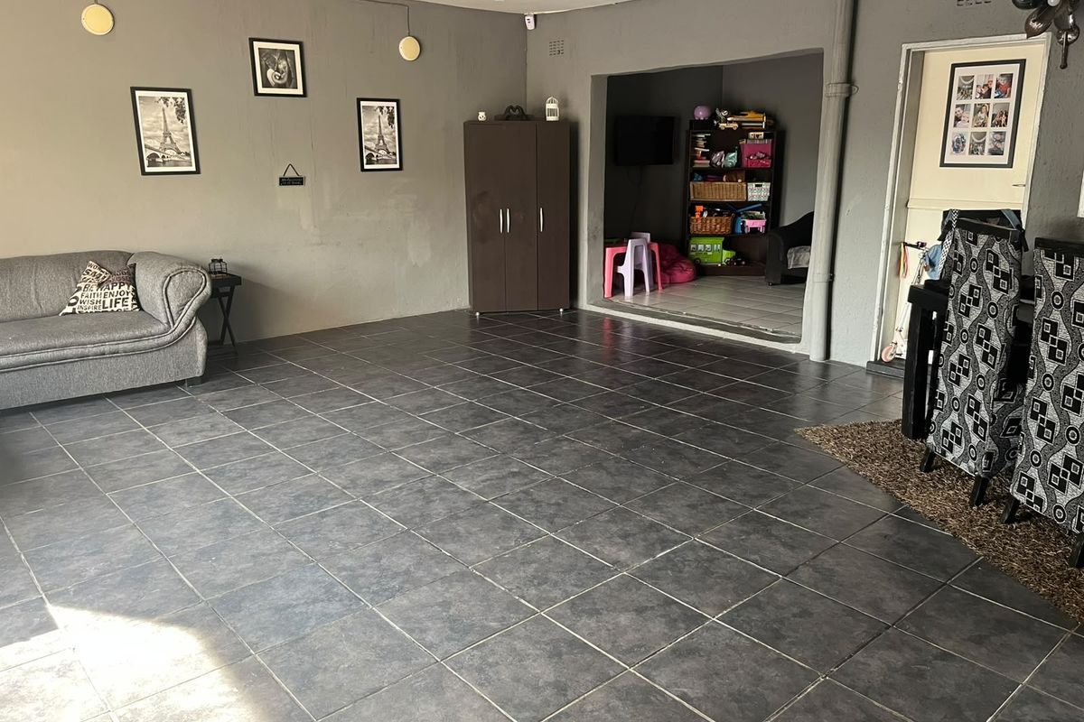Spacious living area featuring dark tiled flooring and neutral grey walls, with an adjacent alcove space and direct access to an internal door.