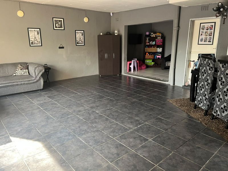 Spacious living area featuring dark tiled flooring and neutral grey walls, with an adjacent alcove space and direct access to an internal door.