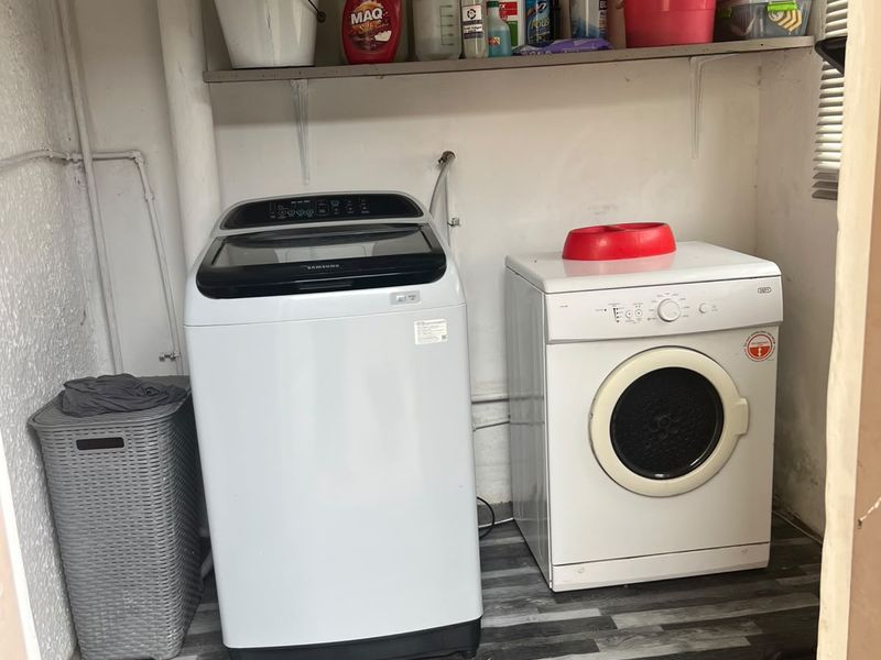 A functional laundry area featuring wall-mounted shelving, vinyl flooring, and dedicated plumbing connections for washing appliances.