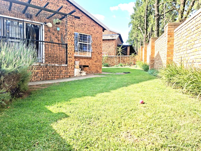 Rear view of the townhouse featuring a face brick facade, a timber pergola over the patio, and a private garden with perimeter walling.