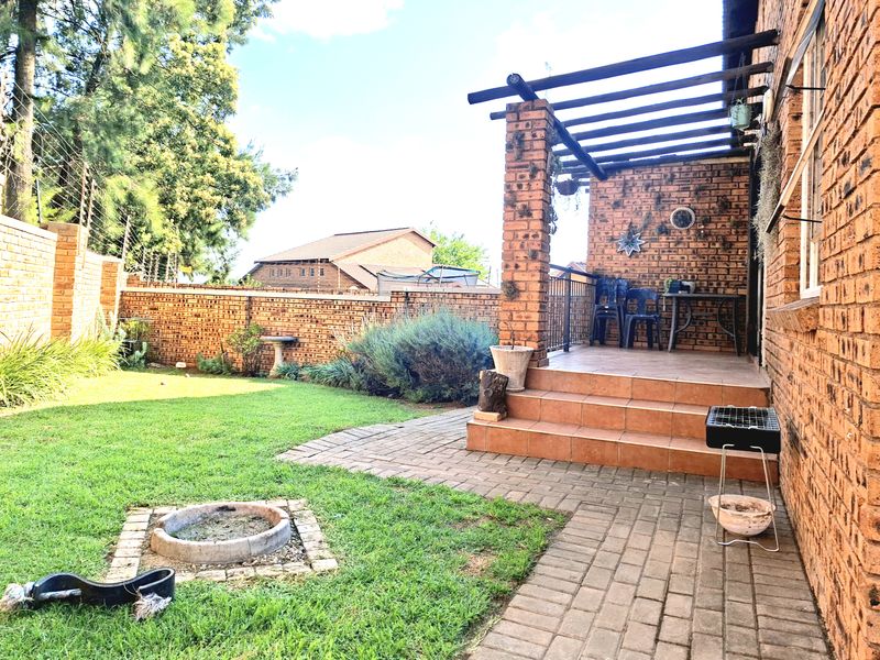 A private rear garden featuring a brick-paved patio with a timber pergola, a built-in fire pit, and a well-maintained lawn enclosed by brick walls.
