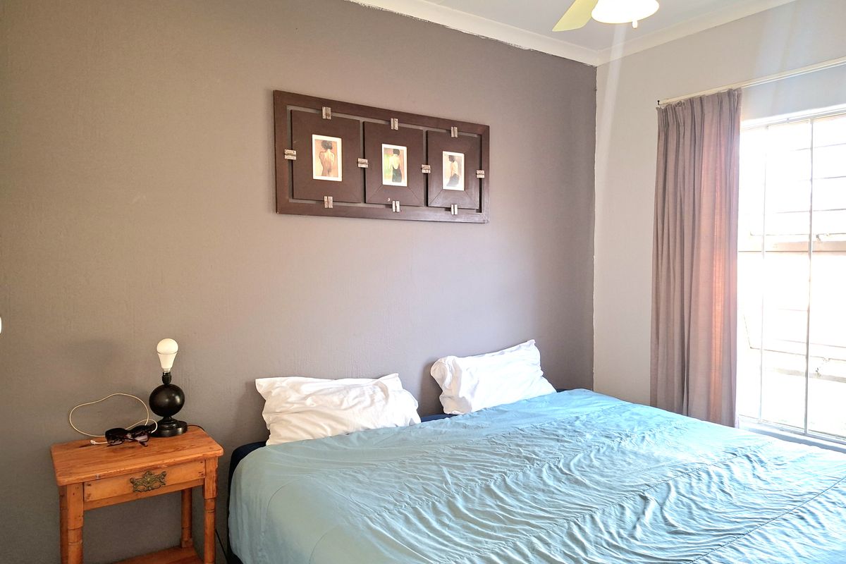 A bedroom featuring a ceiling fan and a window fitted with security bars, finished with a grey accent wall.