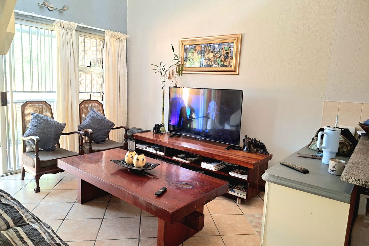 A living room featuring tiled flooring, high ceilings, and a sliding glass door with security gate providing access to the exterior.