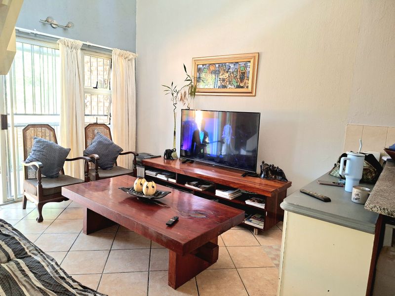 A living room featuring tiled flooring, high ceilings, and a sliding glass door with security gate providing access to the exterior.