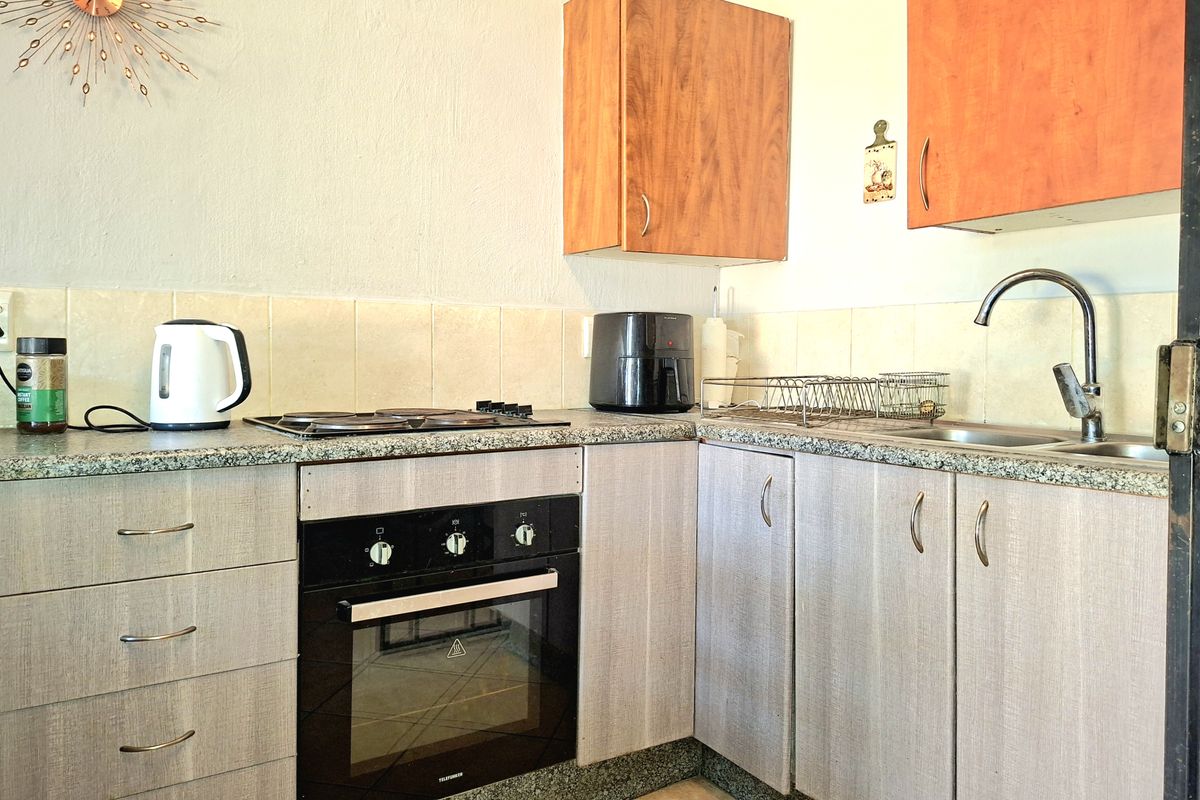 Compact kitchen featuring built-in oven, electric hob, granite countertops, and a mix of wood-tone and grey laminate cabinetry with a tiled backsplash.
