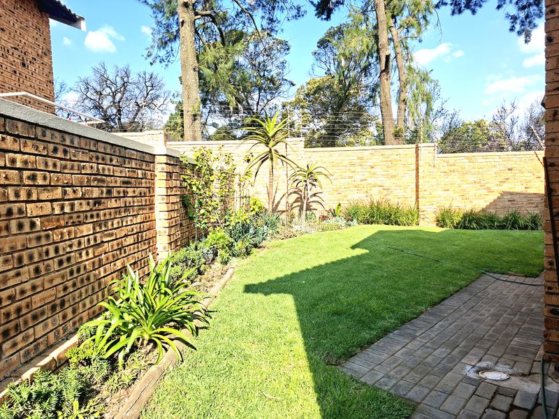 A well-maintained private rear garden featuring a manicured lawn, paved pathway, and secure brick boundary walls with electric fencing.
