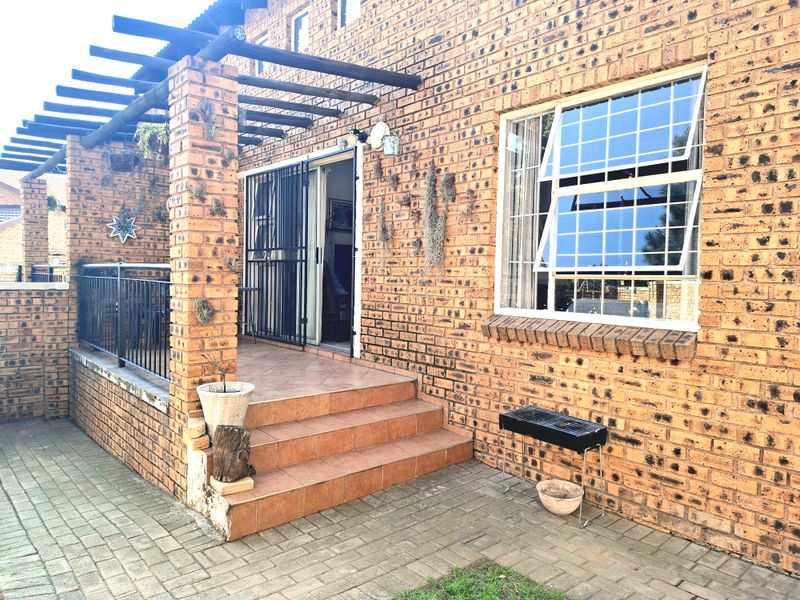 A covered patio area featuring exposed brickwork, a timber pergola, and tiled steps leading to the main entrance of the townhouse.