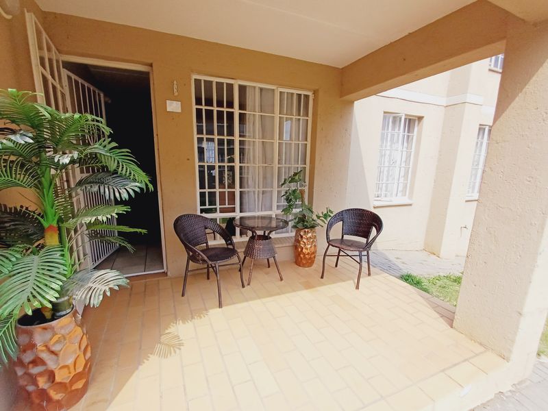 A covered patio area featuring tiled flooring, security gate access, and window grilles, providing a functional outdoor space for the apartment.