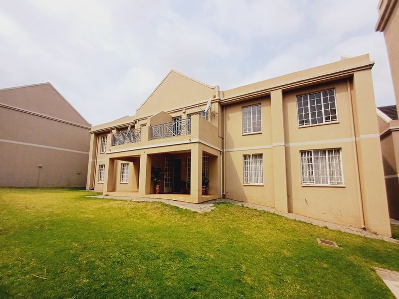 Rear view of a multi-story apartment building featuring a covered patio, upper-level balcony with metal railing, and landscaped lawn area.