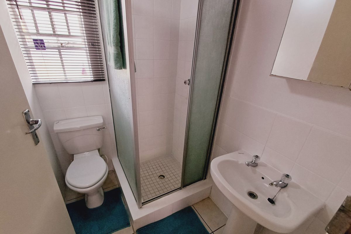 Compact bathroom featuring a shower enclosure, pedestal basin, and toilet with tiled finishes and natural light from a window with blinds.