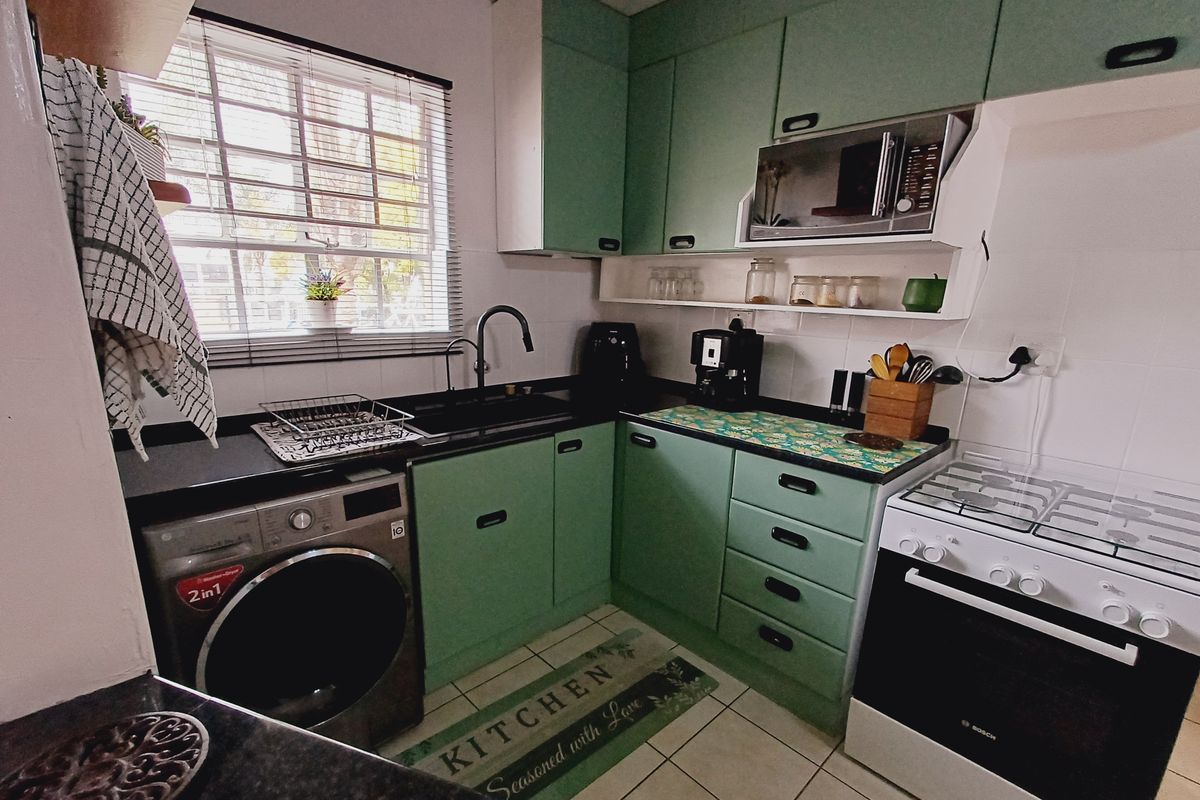 A functional kitchen featuring green cabinetry, dark countertops, a gas stove, built-in microwave, and tiled flooring with a window providing natural light.