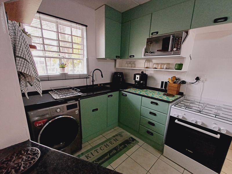 A functional kitchen featuring green cabinetry, dark countertops, a gas stove, built-in microwave, and tiled flooring with a window providing natural light.