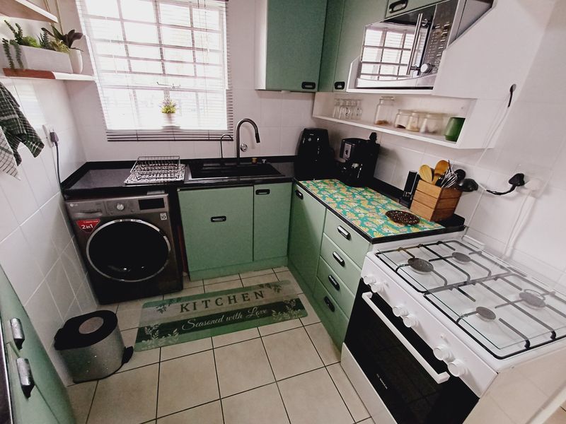 Compact kitchen featuring green cabinetry, gas stove with oven, built-in microwave, and tiled finishes, providing a functional workspace.