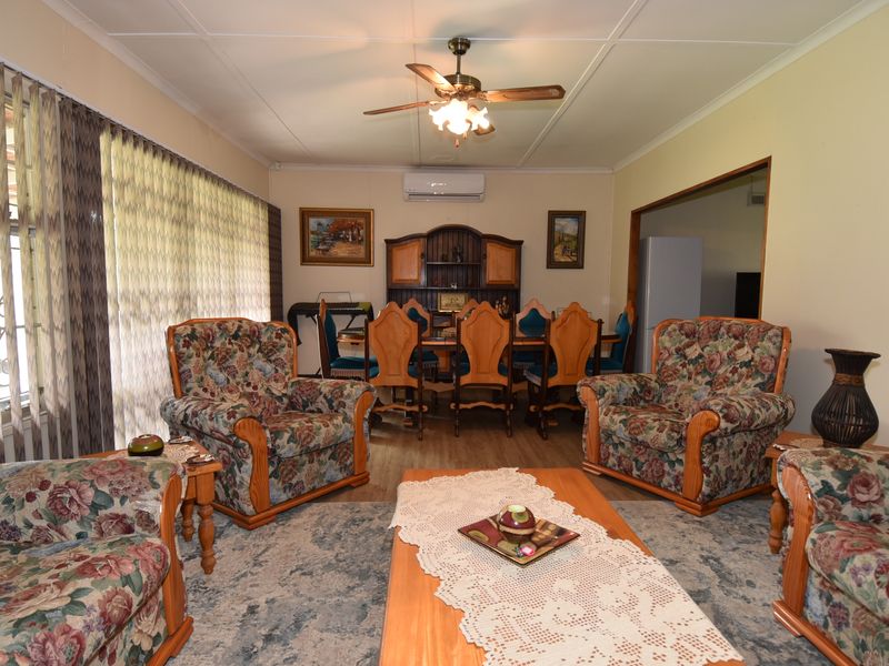 Open-plan living and dining area featuring laminate flooring, a ceiling fan, and a wall-mounted split-system air conditioner.