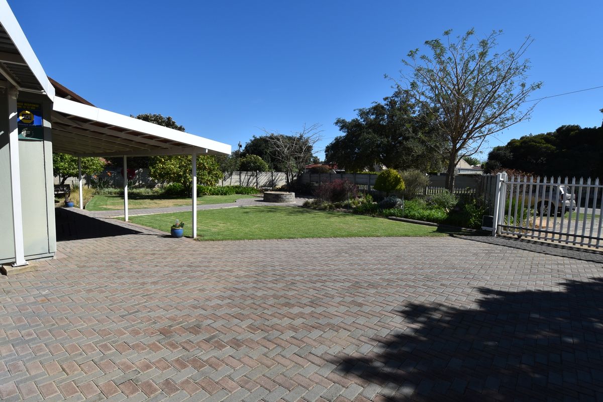Spacious rear garden featuring a paved driveway, covered patio area, well-maintained lawn, and a built-in fire pit.