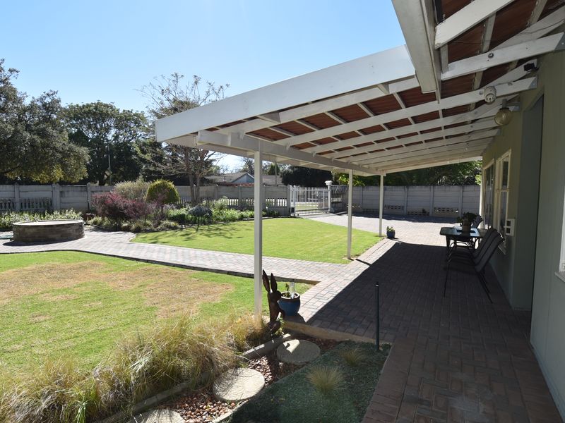 A spacious covered patio overlooking a well-maintained garden with a paved walkway, lawn, and a built-in fire pit area.