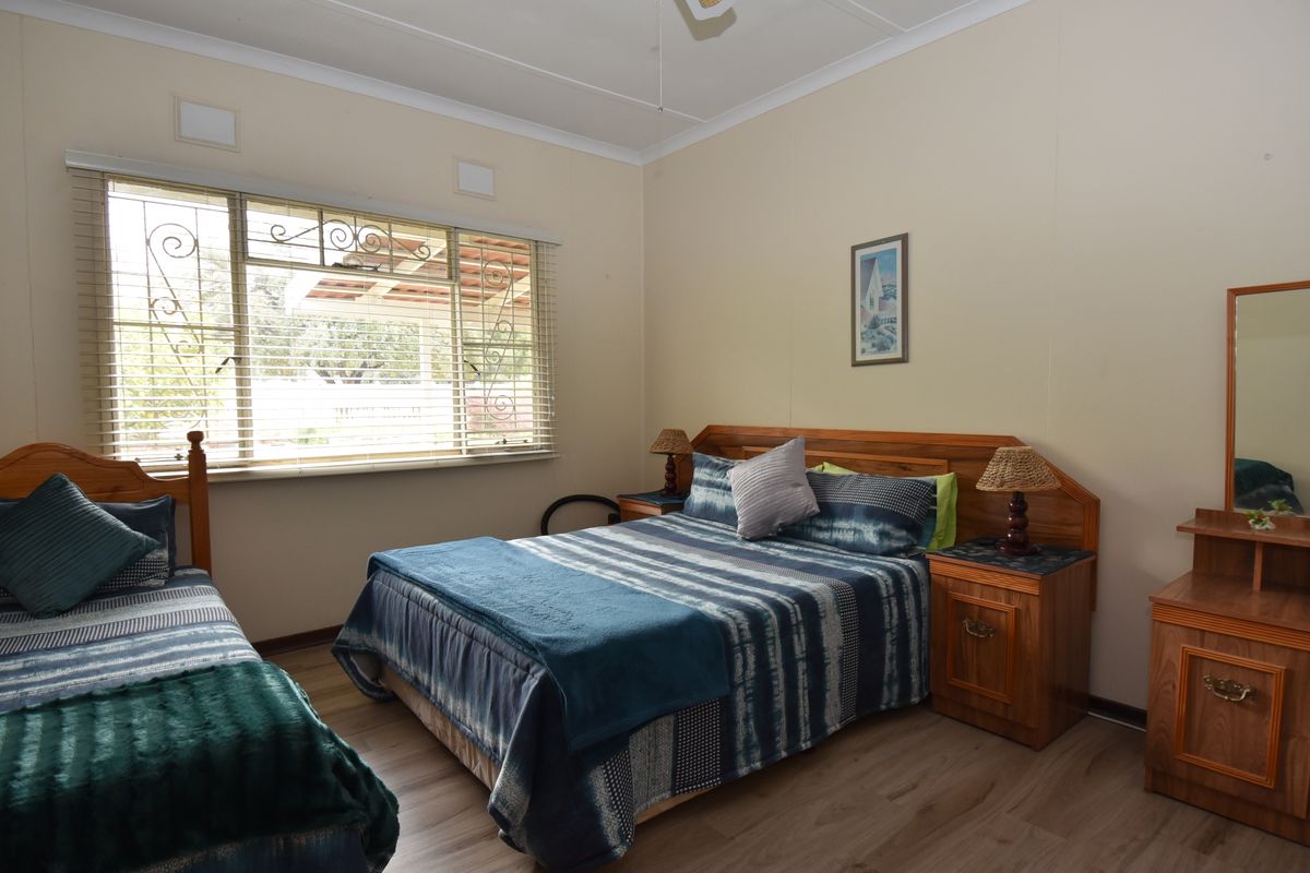 A well-lit bedroom featuring laminate flooring, a ceiling fan, and large windows fitted with security bars and venetian blinds.