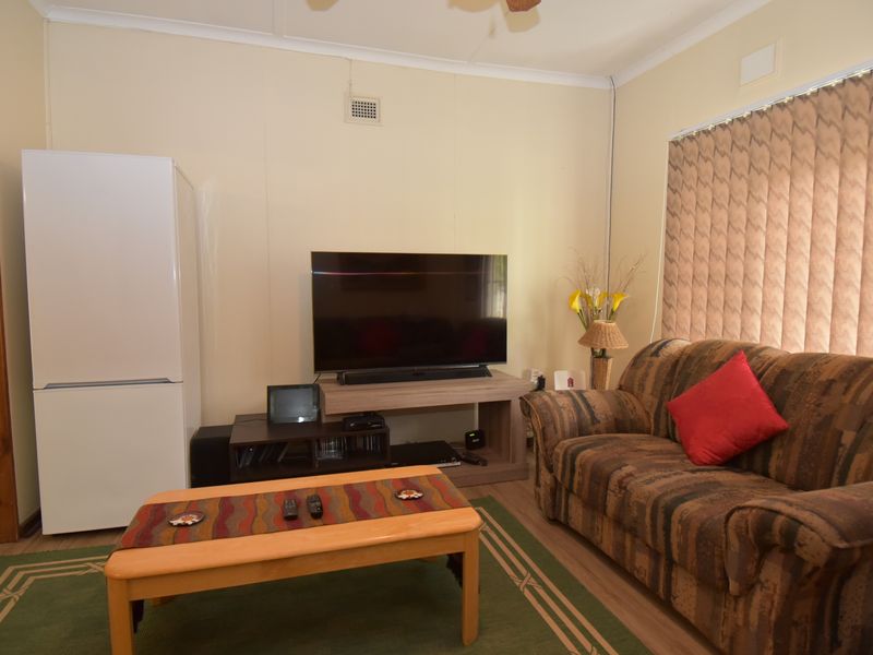 A functional living room featuring laminate flooring, vertical blinds, and a ceiling fan, offering a comfortable and practical space for relaxation.