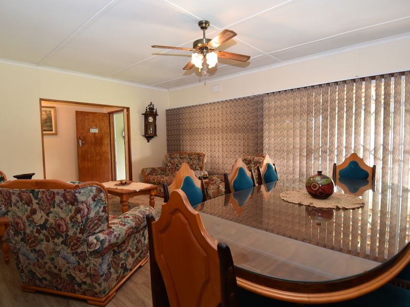 A spacious living and dining area featuring a ceiling fan, vertical blinds, and neutral wall finishes, offering a functional layout for family living.